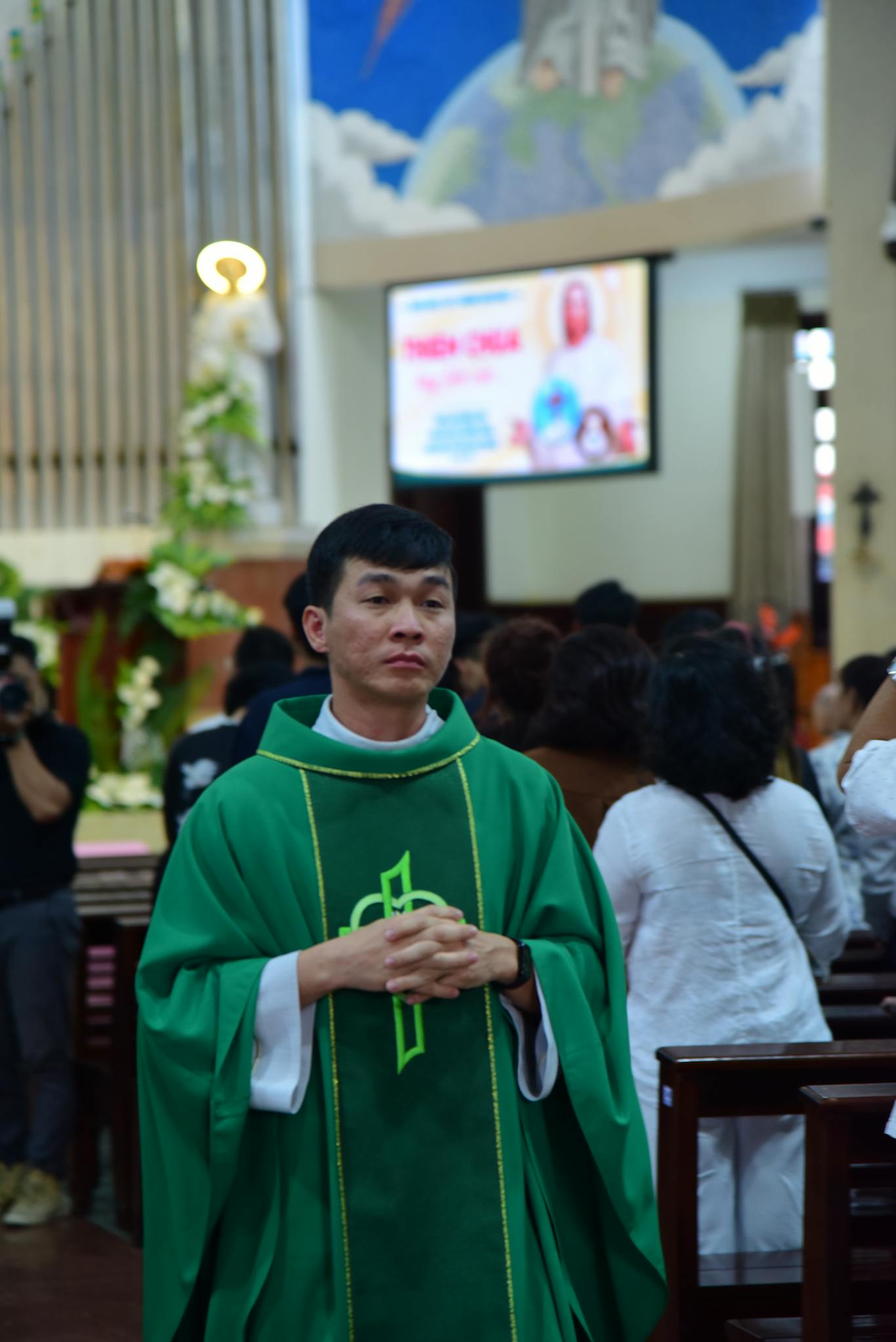 Catholic priest in green vestments leading a church procession indoors.
